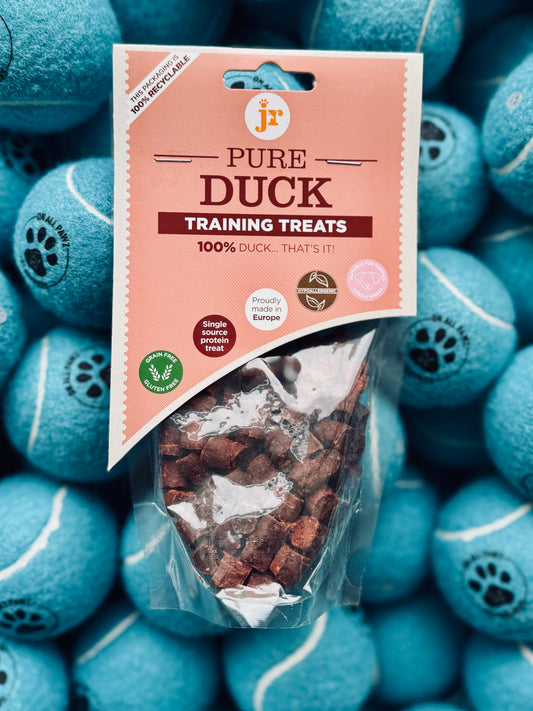 A package of Pure Duck Training Treats placed on a background of blue dog toys, showcasing the treats as a healthy, protein-packed snack for dogs.