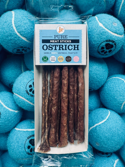 Package of Pure Meat Sticks Ostrich surrounded by blue tennis balls with a visible brand logo.
