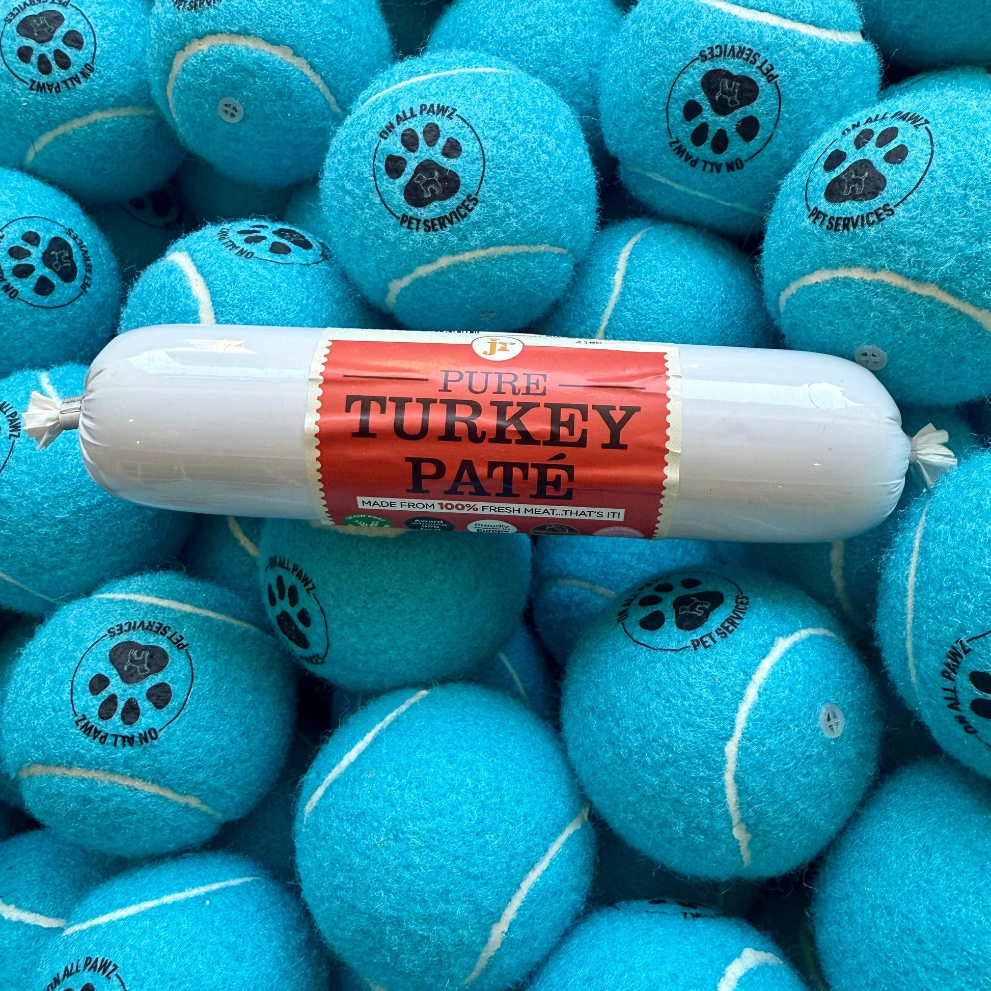 Turquoise tennis balls with paw prints and a package of Pure Turkey Pate on top.