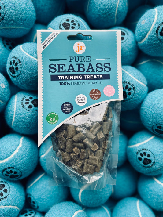A package of Seabass Training Treats placed against a background of blue tennis balls, with the treat visible through the transparent packaging.