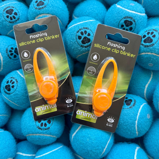 Two orange silicone clip blinkers in packaging surrounded by blue tennis balls.