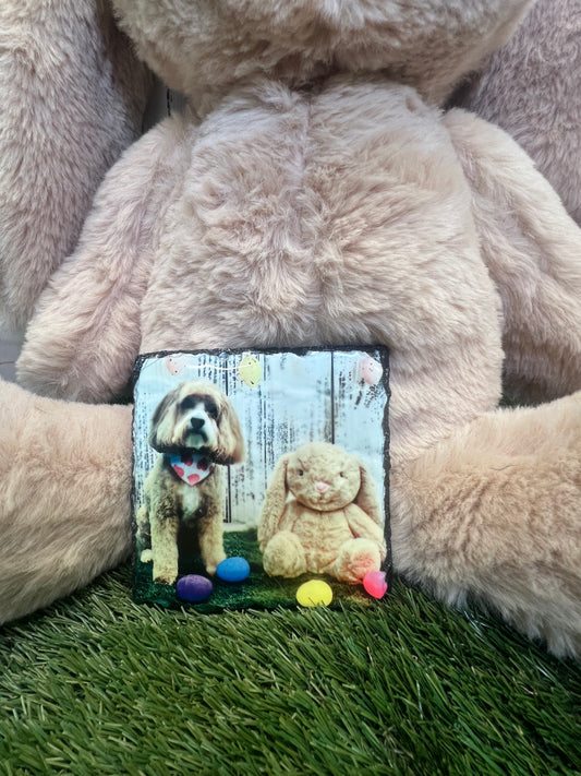 A personalized square coaster with a photo of a dog printed on it, placed on a brown fuzzy surface, likely a pet bed.
