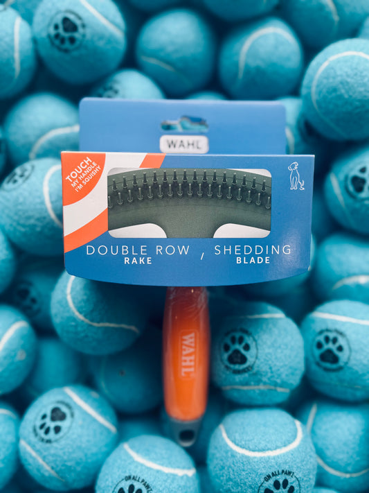 A Wahl brand pet grooming tool, featuring a double row rake and shedding blade, with a comfortable gel handle, packaged in a blue and orange cardboardscroll up icon.