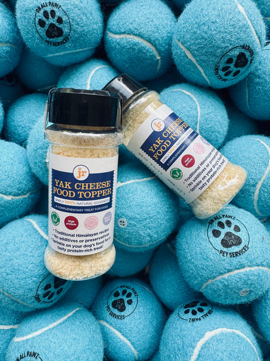 Two bottles of Yak Cheese Food Toppers on a pile of blue tennis balls with paw prints.
